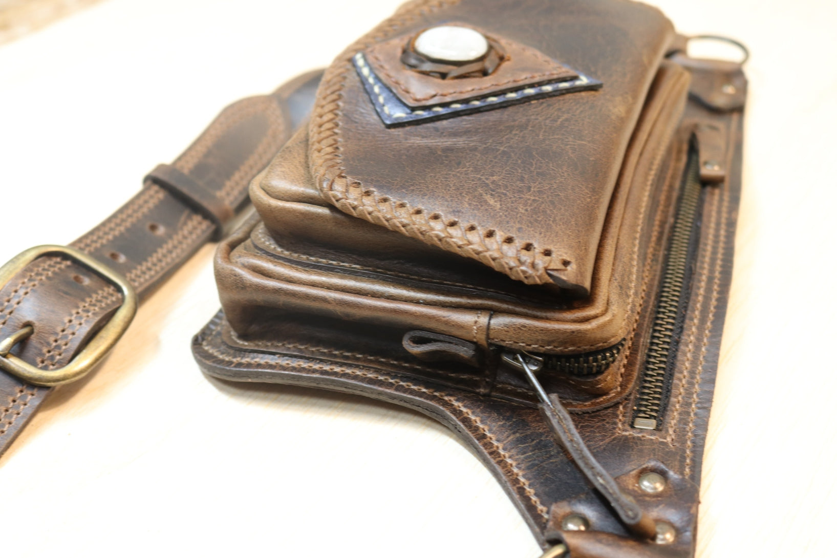A close-up of a dark brown distressed leather belt bag with multiple zippered compartments, a snap-button flap, and a matching leather belt with a brass buckle.