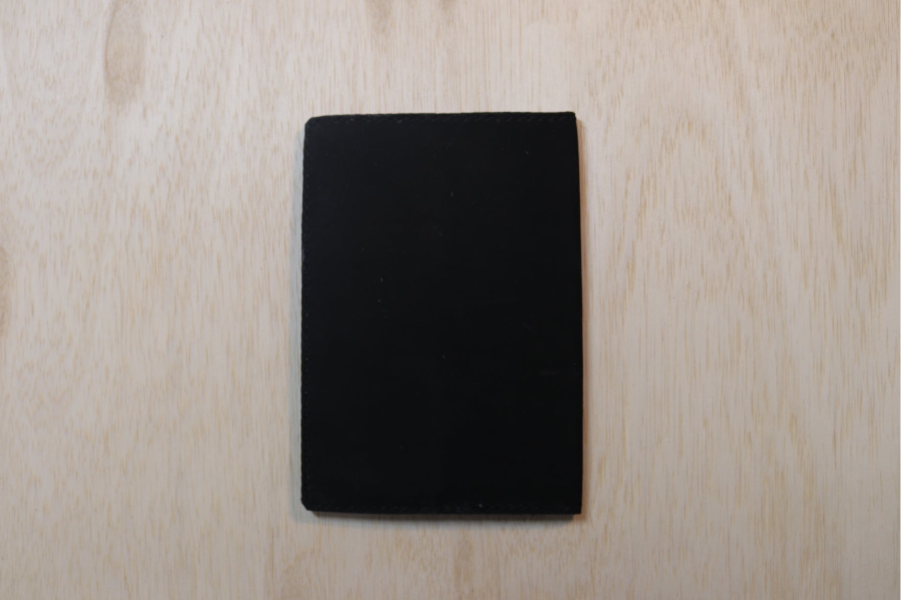 A solid black rectangular card or coaster with rounded corners, centered on a light-colored wood grain background.