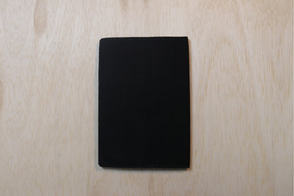 A solid black rectangular card or coaster with rounded corners, centered on a light-colored wood grain background.
