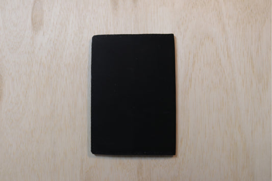 A solid black rectangular card or coaster with rounded corners, centered on a light-colored wood grain background.